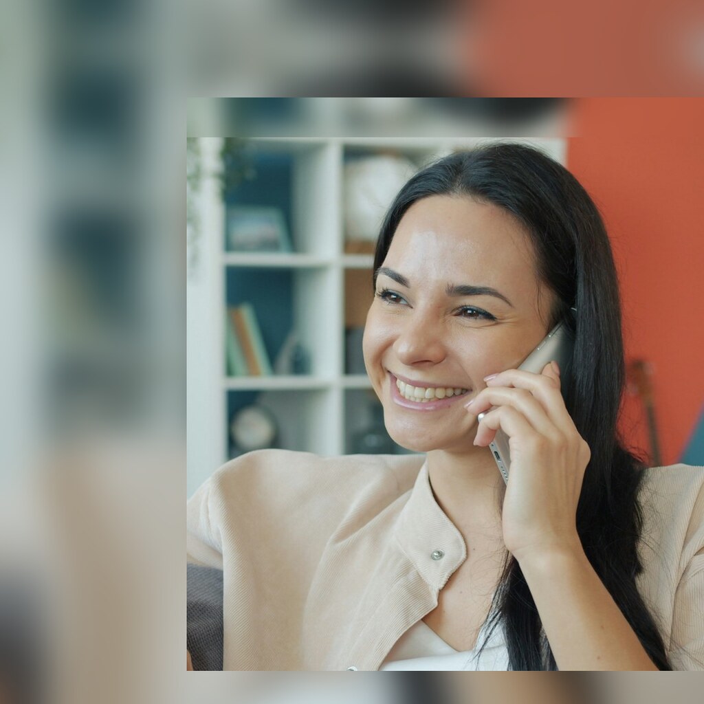 A smiling woman talking on the phone in a bright living room