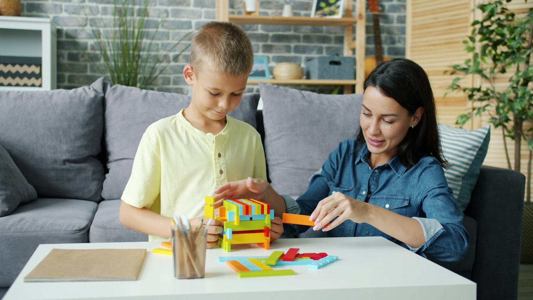 A therapist and a young boy building a colorful wooden block tower together during a play-based session